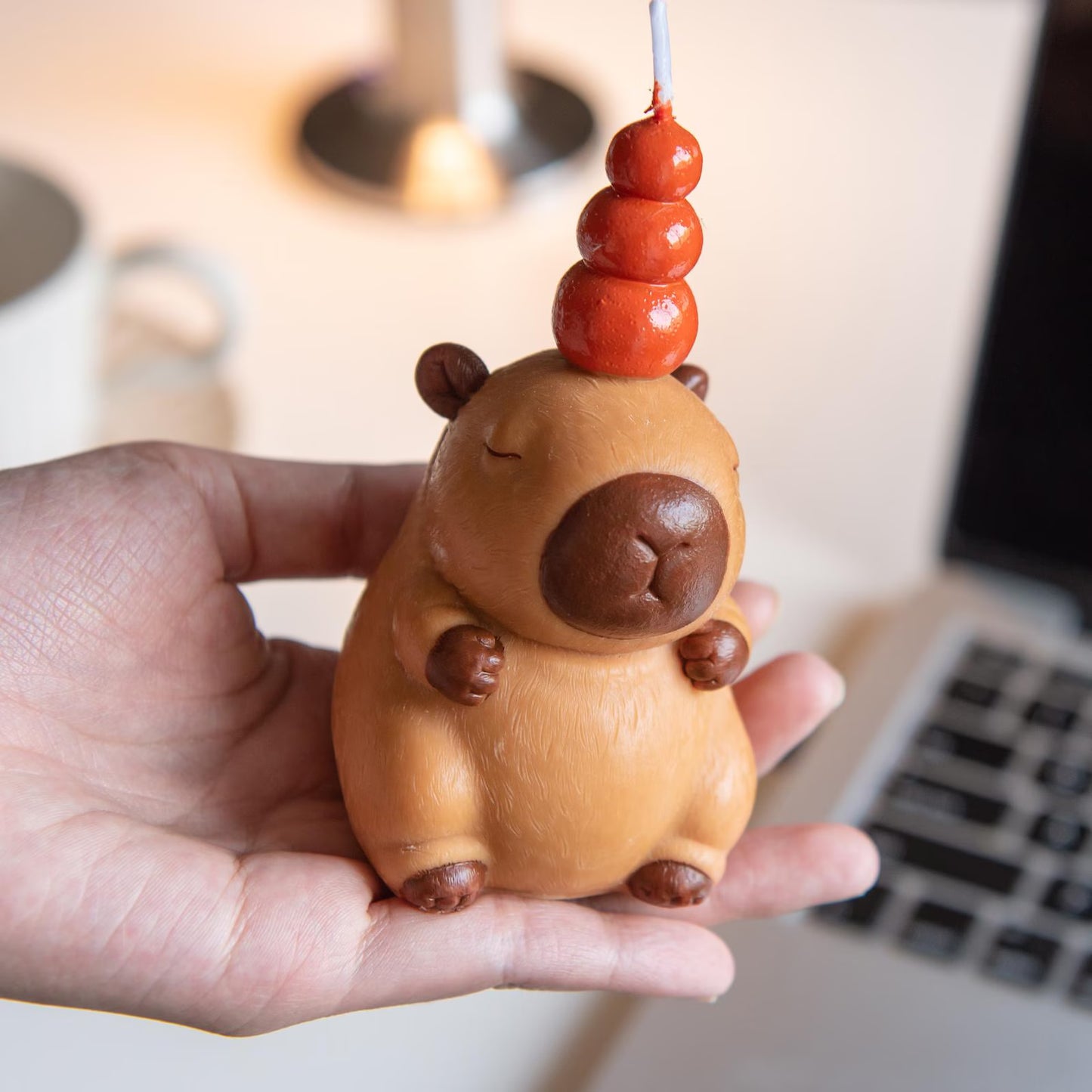 Hand holding a capybara birthday candle with a three-tiered orange wax decoration on top