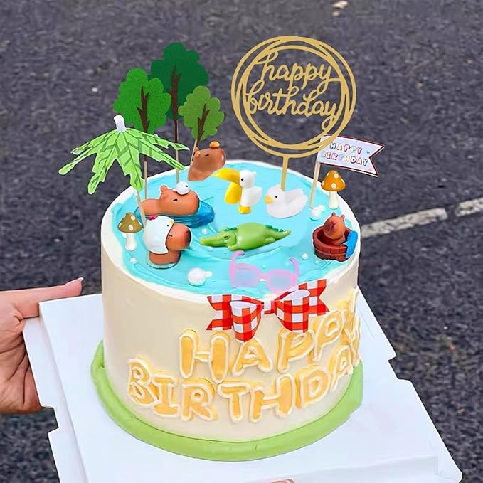 Capybara cake toppers set on a birthday cake with trees, ducks, and a happy birthday sign