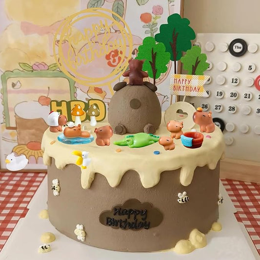 Capybara cake toppers set on a birthday cake with water, trees, and happy birthday sign decoration