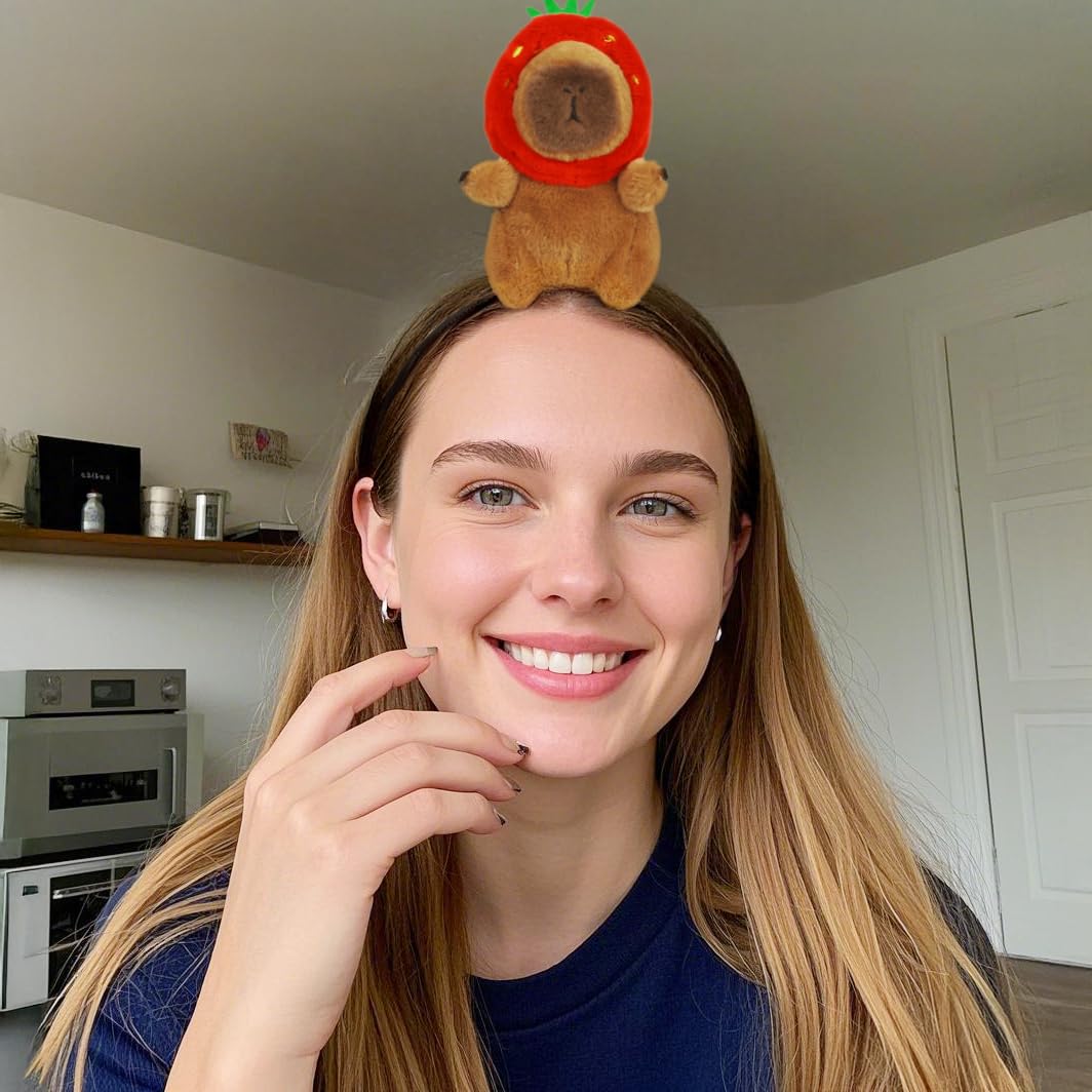 Smiling woman wearing a capybara headband accessory with a plush capybara in a red fruit costume on her head