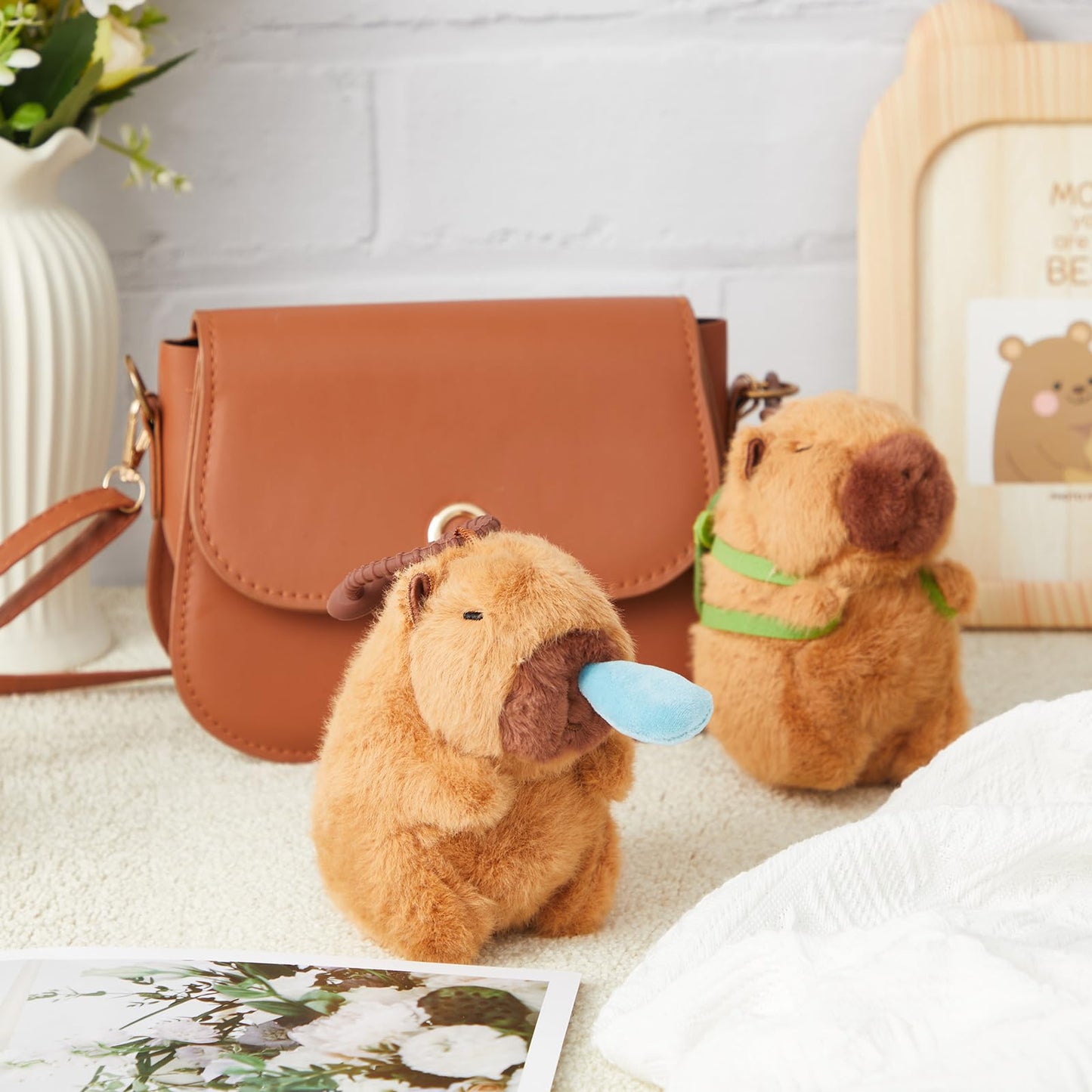 brown capybara plush keychain with blue tongue and green scarf displayed near a brown handbag