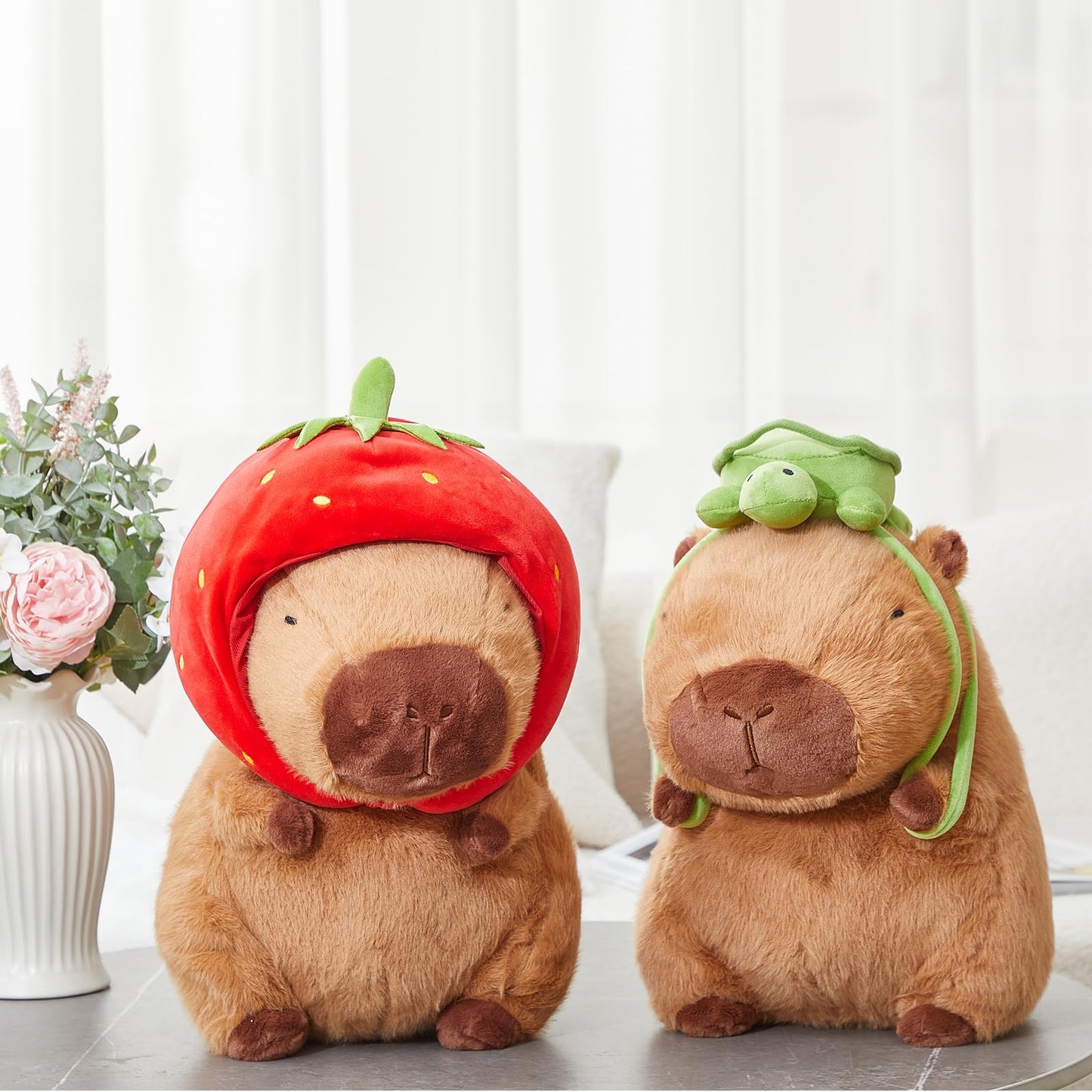 capybara plush toy set featuring two soft brown capybaras with a red strawberry hat and a green frog hat