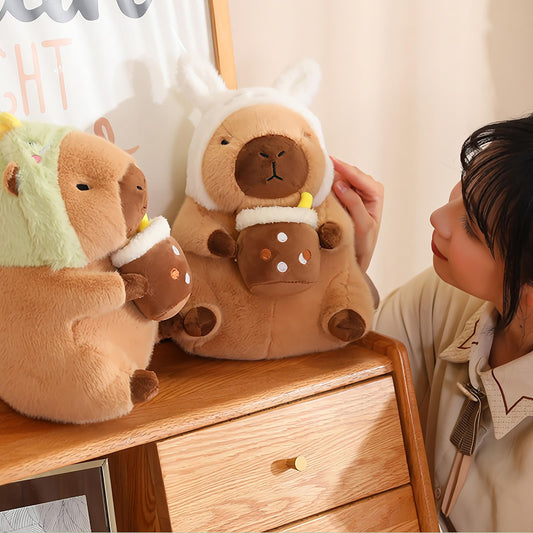 capybara plush toy with dinosaur hood holding a cup and child playing with the stuffed animal
