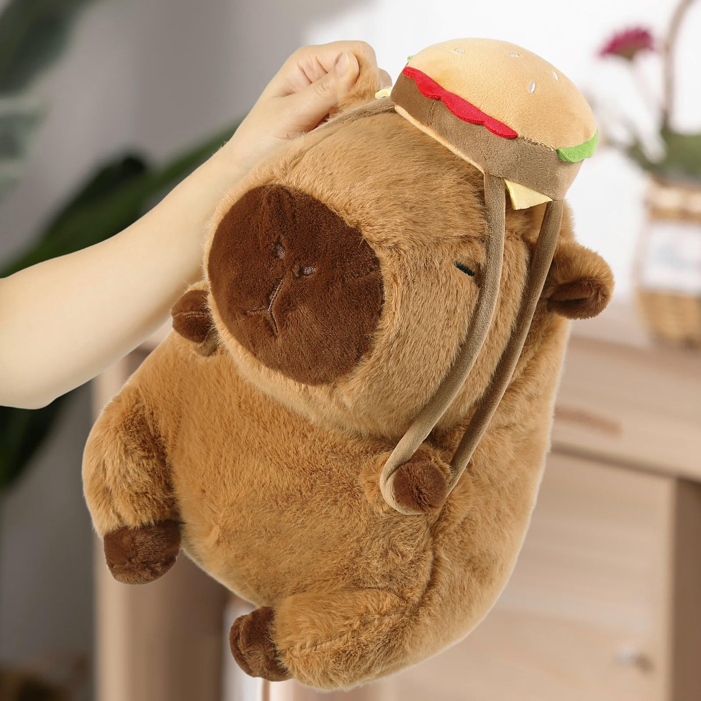 capybara plush toy with hamburger backpack held by hand in room setting