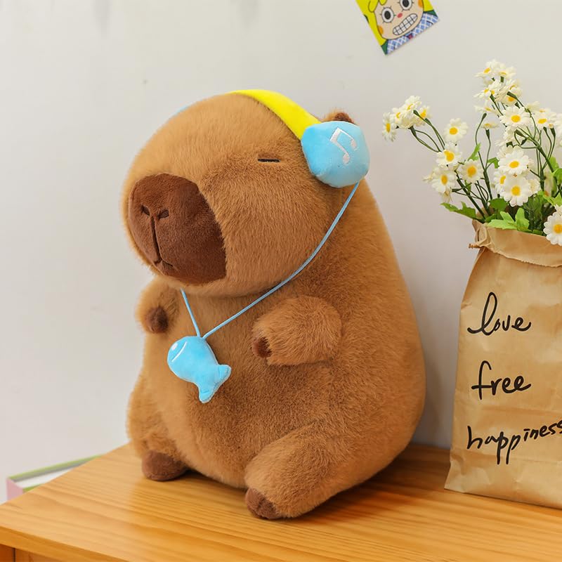 Cute brown capybara plush with headset featuring blue headphones and fish pendant sitting on wooden surface