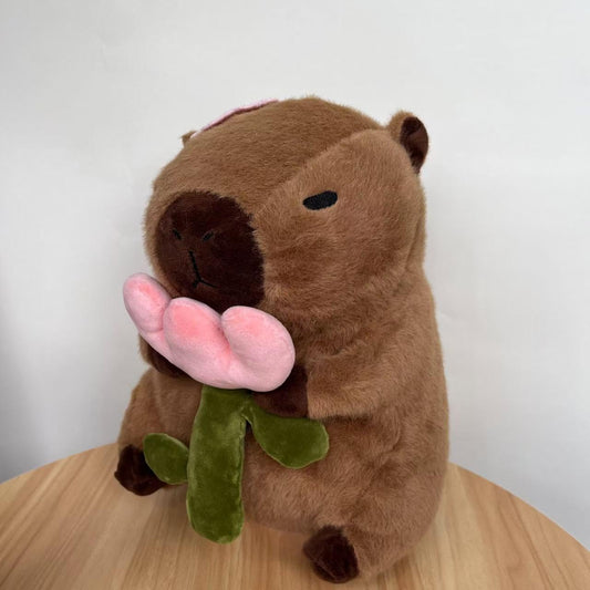 capybara plush with rose holding a pink flower with green stem and leaves
