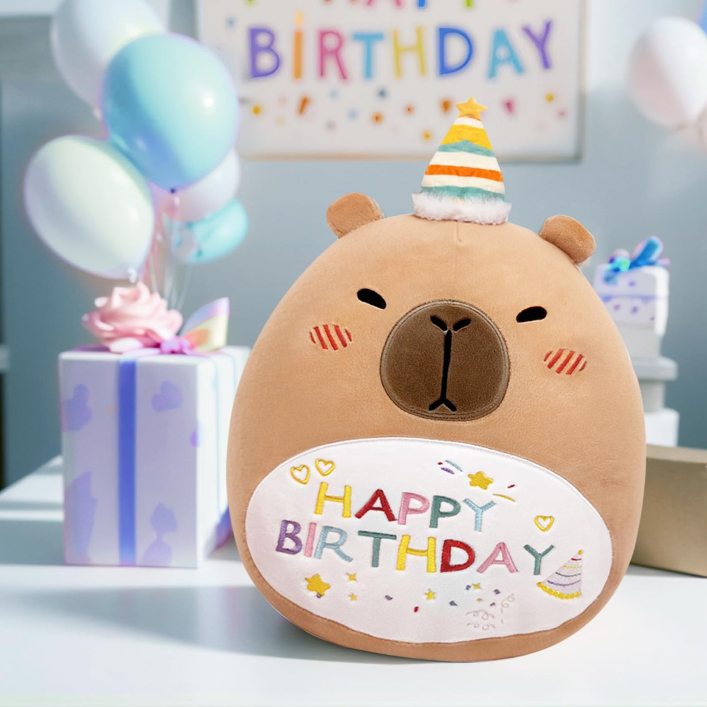 Cute capybara plush pillow wearing a party hat with happy birthday embroidery on a table