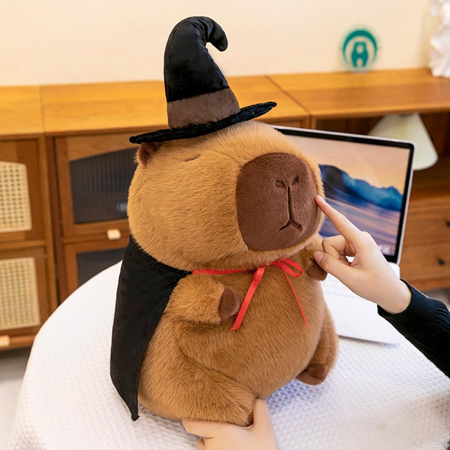 cute wizard capybara plush wearing a black wizard hat and cape, held on a table indoors