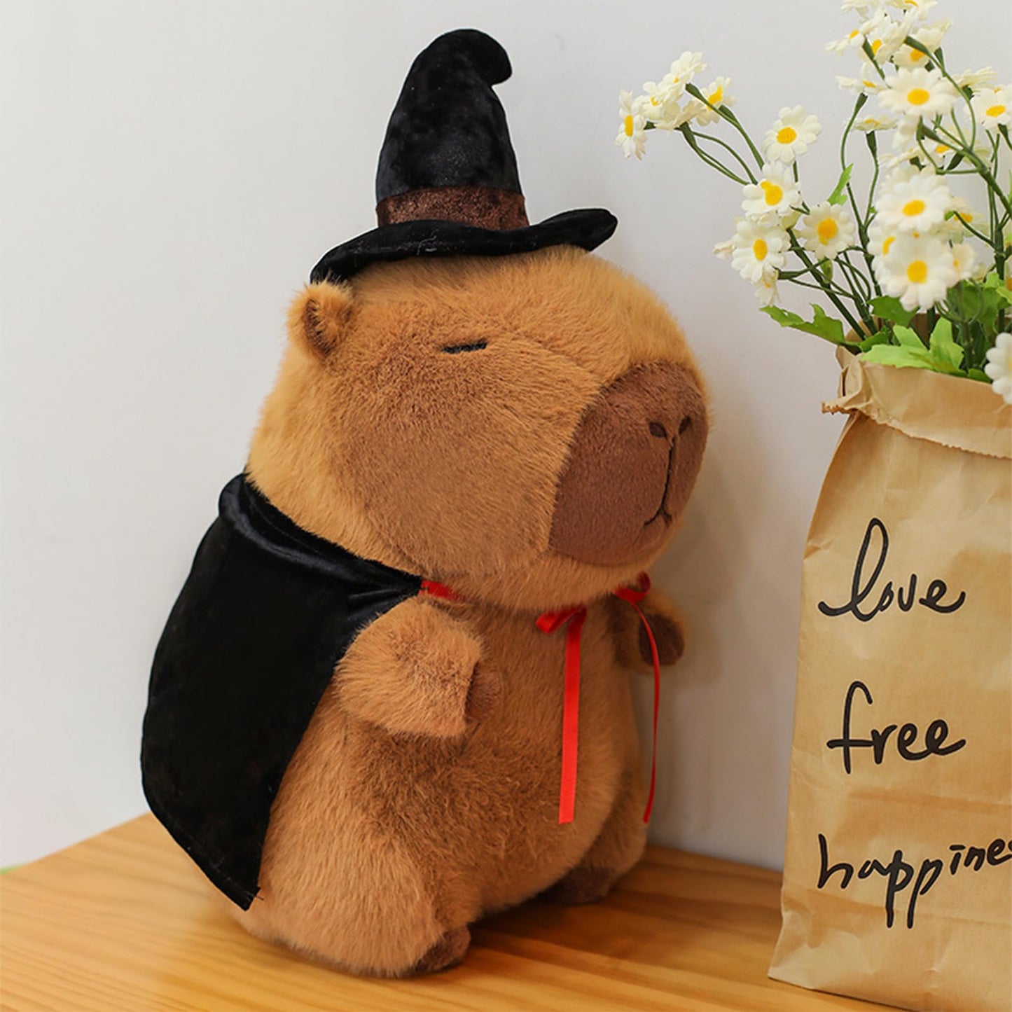 Cute wizard capybara plush wearing a black wizard hat and cape sitting on a wooden surface