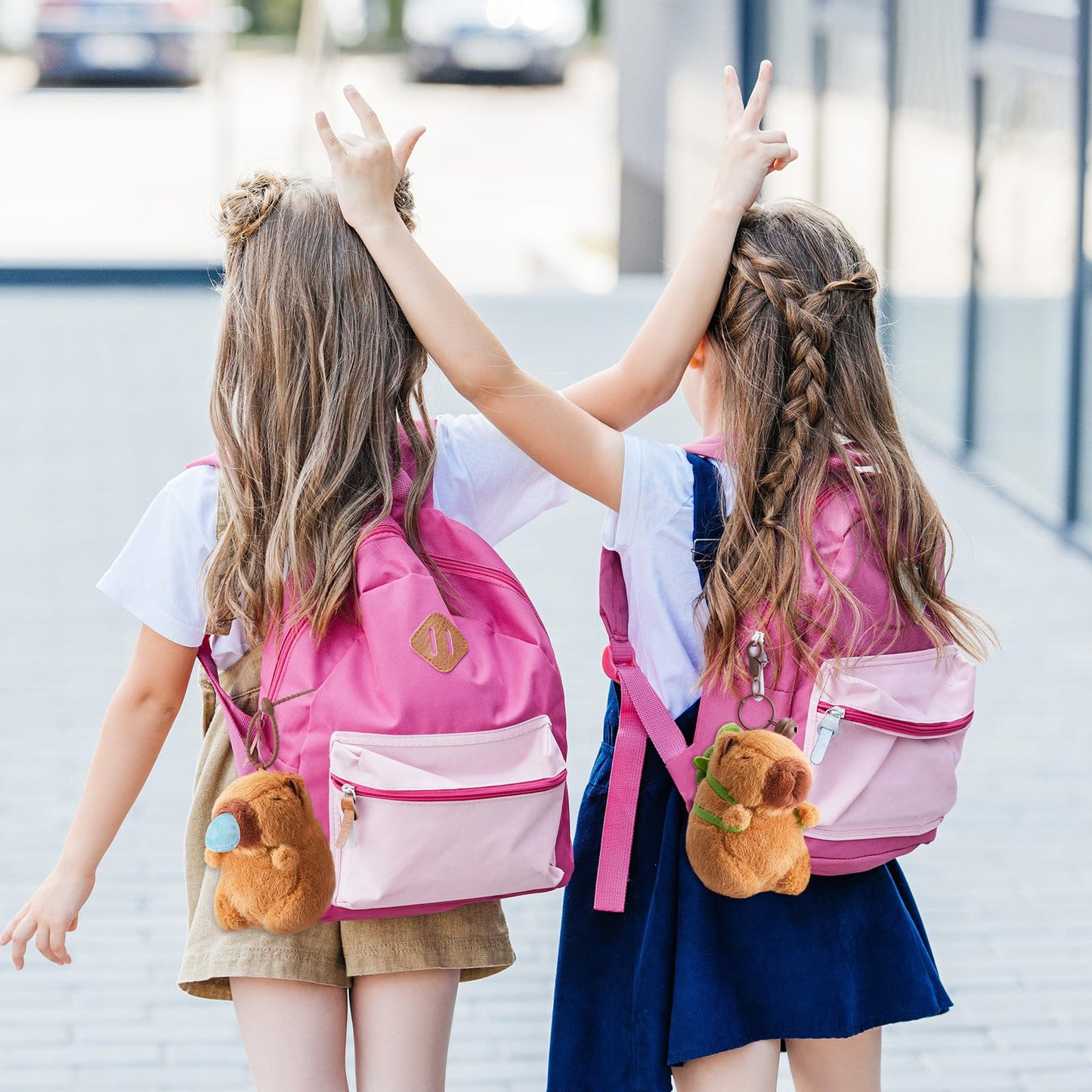Two girls wearing pink backpacks with Simgoing capybara plush keychain attached outdoors