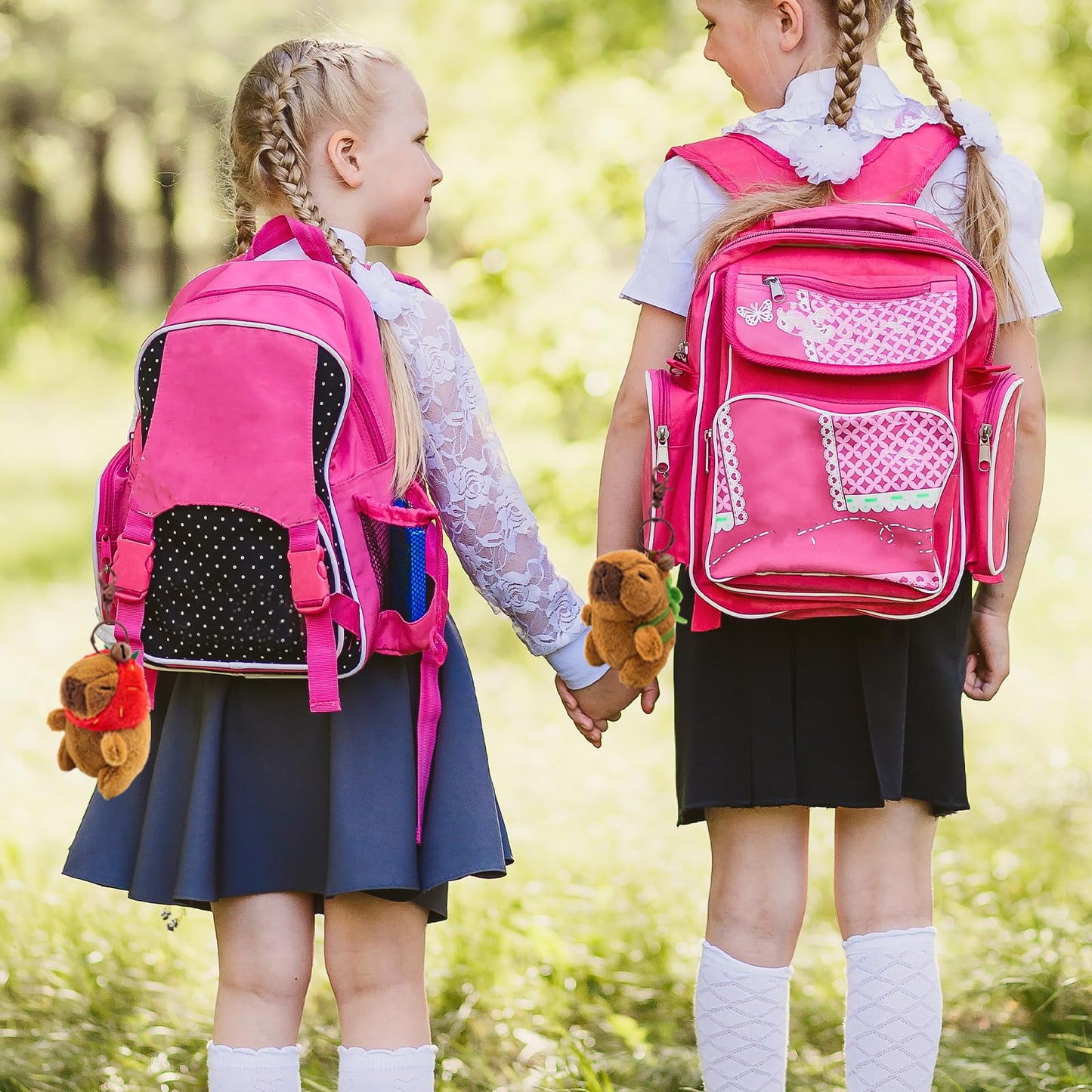 Two schoolgirls holding hands with pink backpacks featuring plush capybara keychain 4 pack attached
