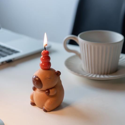 MrsCapybara capybara birthday candle lit on desk near coffee cup and laptop
