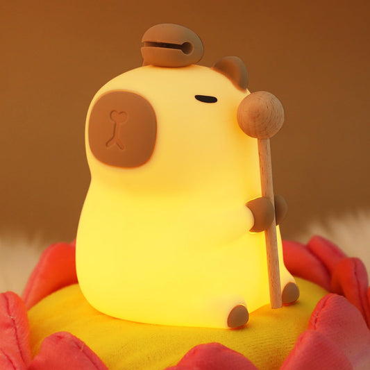 capybara night light glowing warmly while holding a wooden stick on a soft flower cushion
